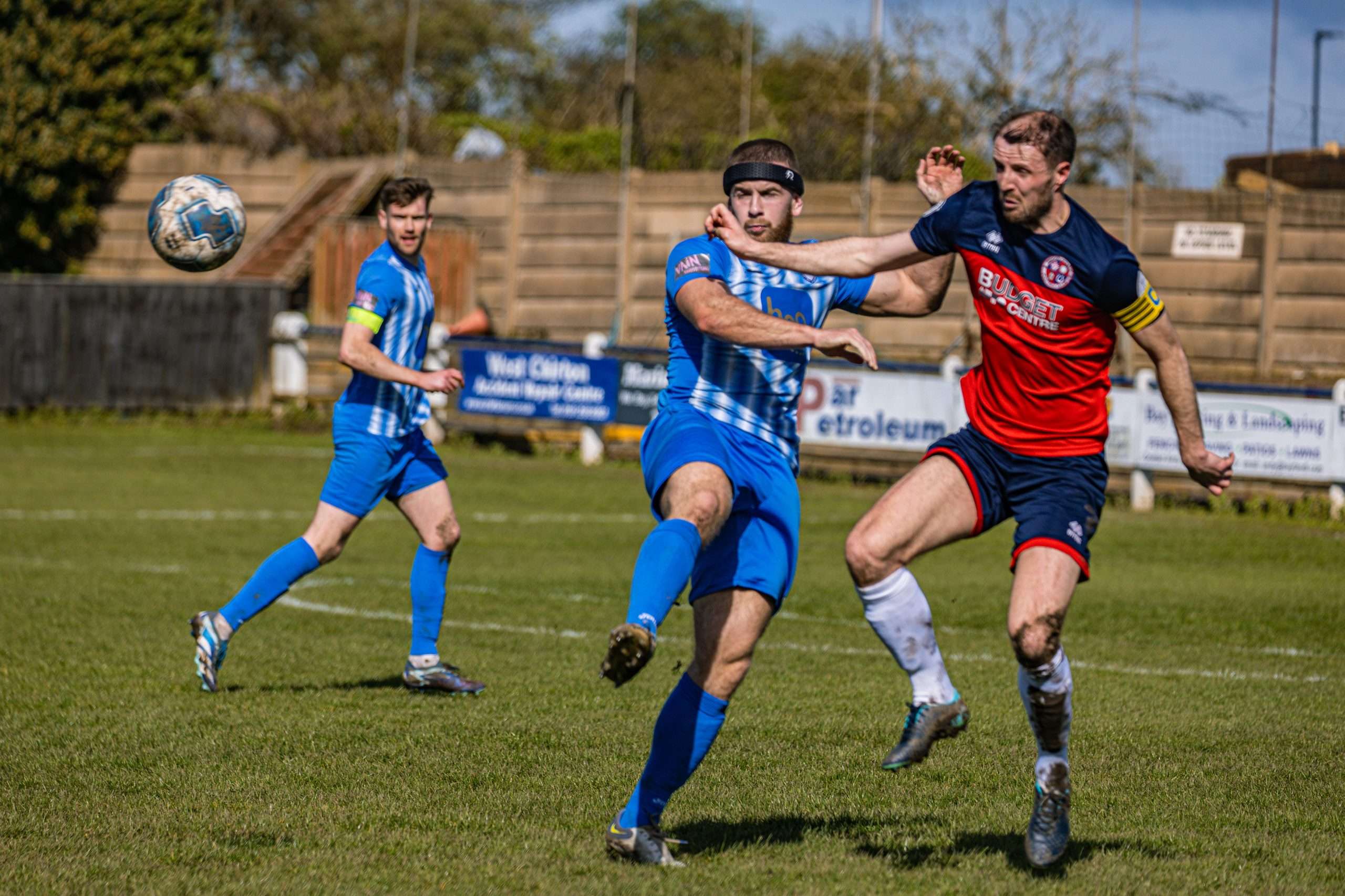 Image shows two football players competing for the ball. The player in blue is wearing Rezon Halos® brain protection and is being pushed in the shoulder by the player in red.